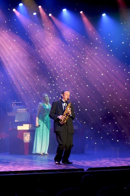 Tim Fulker performing saxophone on stage under spotlights in black tie