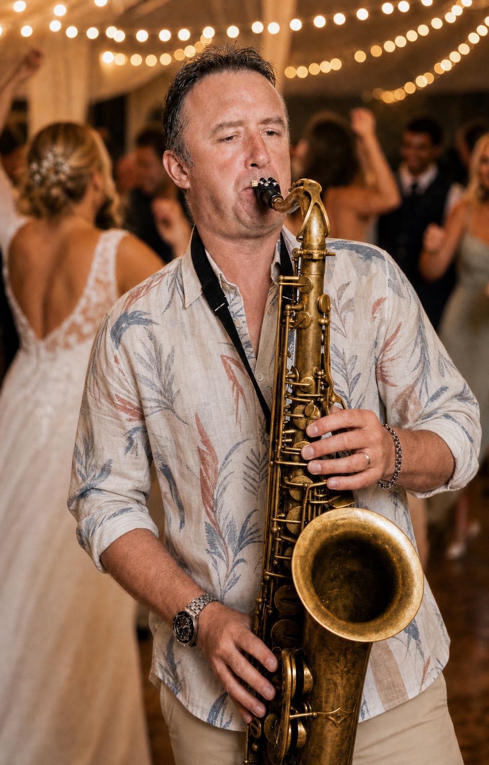 Tim Fulker playing live saxophone on the dance floor at a wedding, string lights above